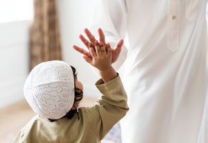 muslimischer Junge schlägt freundschaftlich seine Hand auf die Hand seines Erziehers. Der Junge trägt islamische Kleidung