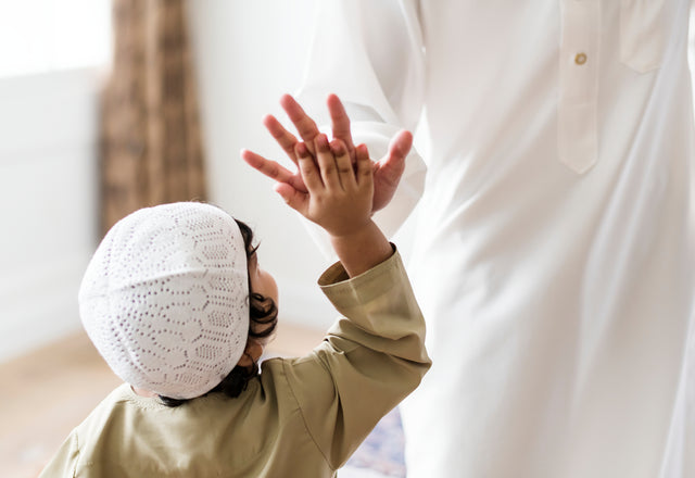 muslimischer Junge schlägt freundschaftlich seine Hand auf die Hand seines Erziehers. Der Junge trägt islamische Kleidung